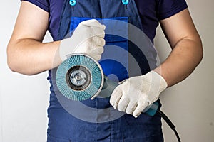 Angle grinder in the hands of a working man against the background of blue overalls. Industry