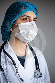 Angle portrait of a young female doctor wearing medical mask, gown and stethoscope. Nurse waiting for the next patient