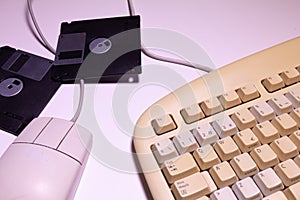 Angle top view of an old computer keyboard, a mouse with their wires and some floppy disks on a white background