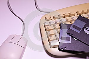 Angle top view of an old computer keyboard, a mouse with their wires and some floppy disks on a white background