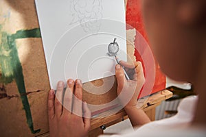 Angle View of a arist`s hand drawing on a white paper in front of easel. Closeup