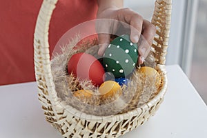 Angle view of colored easter eggs on fluffy dried grass in big basket, boy holds green egg.