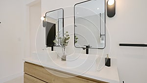 Angle view on contemporary bathroom with two modern sinks, stylish framed mirrors and black wall lights. Minimalist