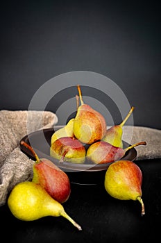 Angle view of fresh pears in clay plate with sackcloth on dark background. Colorful still life in rustic style.