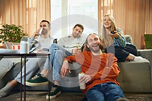 Angle view of a happy group of friends sitting on the sofa in the living room and watching a football match
