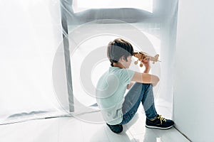 Angle view of kid with dyslexia sitting on floor and playing with wooden plane