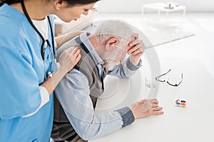 Angle view of nurse putting hands on sad and grey haired man