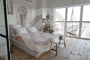 Angle view on spacious white bedroom with big windows decorated with Christmas New year tree and tea