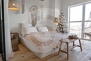 Angle view on spacious white bedroom decorated with Christmas New year tree and tea set standing on a bench