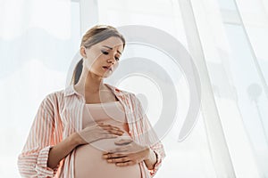 Angle view of worried pregnant woman touching belly and looking down