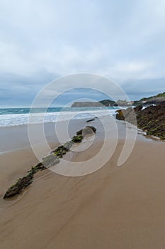 Angled perspective of beach with rocks, with cloudy and blue sky, in Comillas, Cantabria, photo