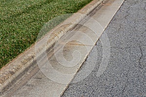 Angled view formed concrete curb, green grass and asphalt street