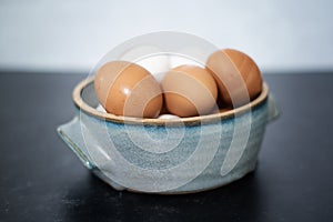 Angled view of handmade ceramic bowl of fresh organic brown and white eggs on dark and concrete background.