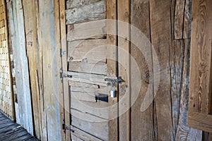 Angled view of a rustic, wooden door with a metal latch and padlock keeping it secure
