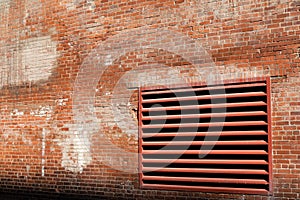 Angled view of weathered brick wall of an old industrial building with large HVAC exhaust vent painted red