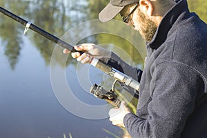 Angler adjusts the brake on the spinning-wheel while standing over the water.
