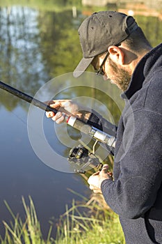The angler adjusts the brake on the spinning-wheel while standing over the water.