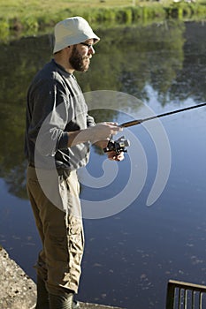 The angler adjusts the brake on the spinning-wheel while standing over the water.