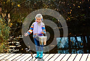 An angler girl with a fishing rod and a bucket with a catch stands on the bridge