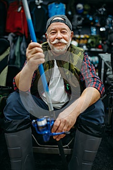 Angler in rubber boots holds rod in fishing shop