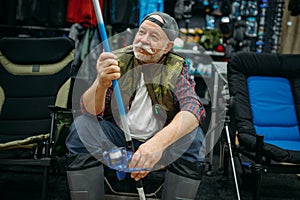 Angler in rubber boots holds rod in fishing shop