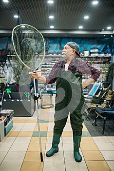 Angler in rubber jumpsuit holds net, fishing shop