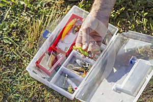 An angler`s rod chooses a spinning bait from the box.