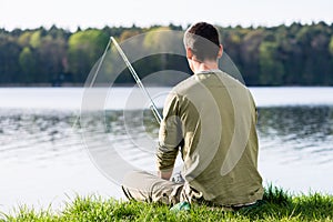 Angler sitting in grass at lake fishing with his rod