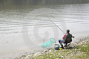 Angler Sitting On The River Coast And Patiently Waiting For Fish To Take A Bait