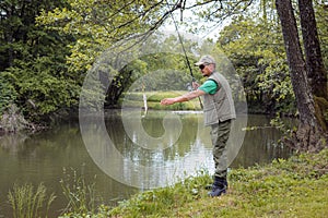 Angler standing on a riverbank and successfully catching a fish photo