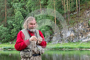 Angler tying fishing hook for fly fishing. fisherman mounts fly on fishing rod