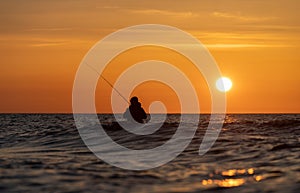 An angler in waterproof trousers fishes in front of a gorgeous orange sunset in the Baltic Sea.