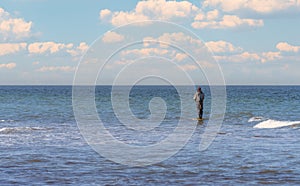 An angler in waterproof trousers is fishing in the Baltic Sea. He is standing on a stone in the water