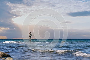 An angler in waterproof trousers is fishing in the Baltic Sea. He is standing on a stone in the water