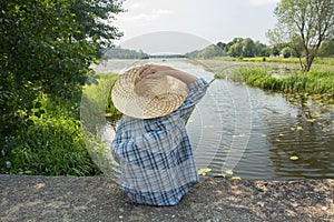 Angling boy with fishing rod holding with one hand straw hat
