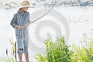 Angling teenage boy looking at handmade green twig fishing rod in his arms