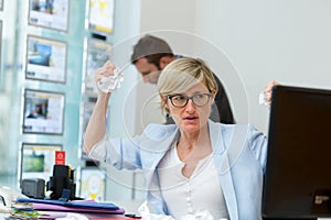 Anglry woman sat at computer scrunching up paper