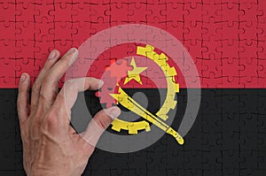 Angola flag is depicted on a puzzle, which the man`s hand completes to fold