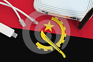 Angola flag depicted on table with internet rj45 cable, wireless usb wifi adapter and router. Internet connection concept