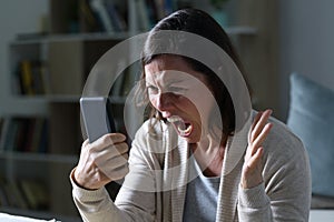 Angry adult woman shouting looking phone at night at home