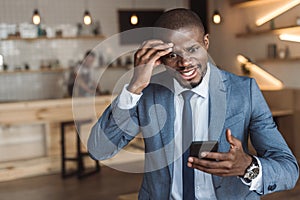 angry african american businessman gesturing and using smartphone