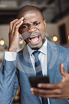 angry african american businessman screaming and using smartphone