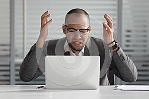 Angry african business man using laptop mad about computer problem photo