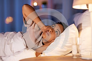 angry african woman lying in bed and closing ears