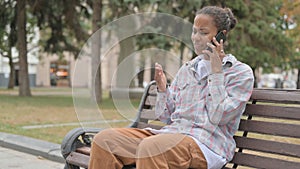 Angry African Woman Talking on Phone while Sitting Outdoor on Bench
