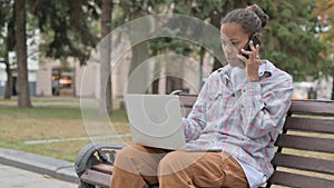 Angry African Woman Talking on Phone and using Laptop, Sitting Outdoor on Bench