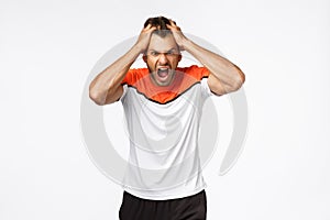 Angry, aggressive mascular sportsman looking furious, grab head in rage and fury, shouting and grimacing from anger and