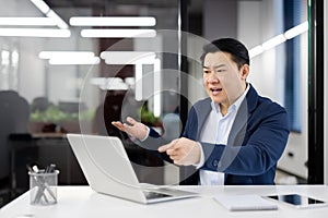 Angry angry boss at workplace inside office, senior mature asian man yelling at interlocutor, businessman using laptop