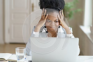 Angry annoyed afro businesswoman screaming, wear headphones talking to a bad customer work on laptop