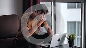 Angry annoyed man screaming and aggressively reacting to what he saw on screen of laptop computer, while sitting on sofa